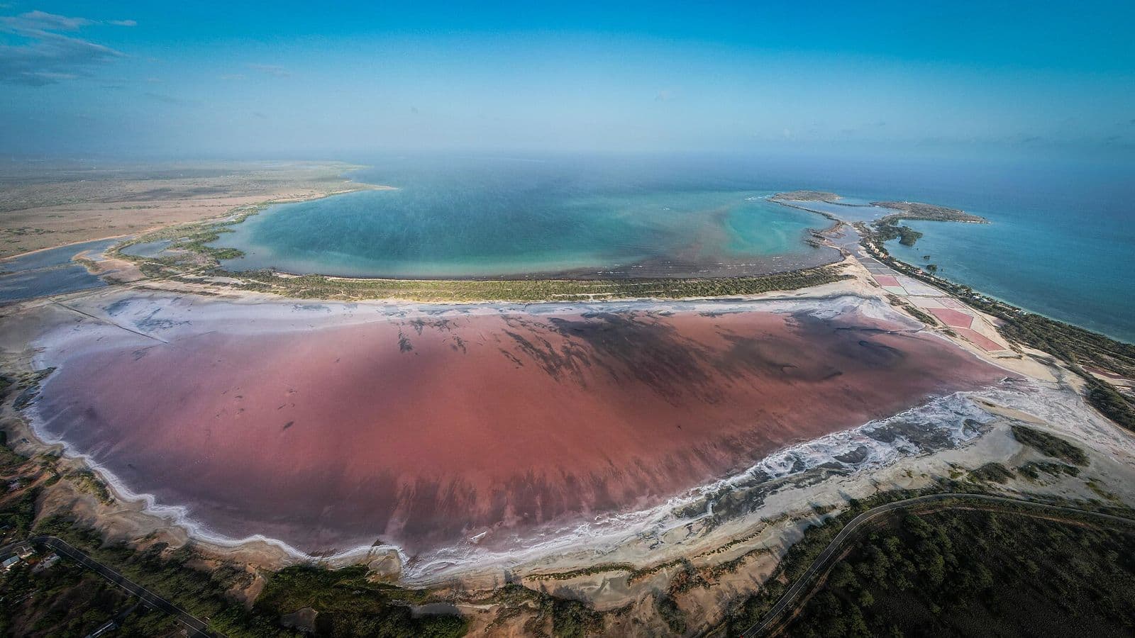 Aerial view of the pink Cabo Rojo salt flats edged with white salt, with a turquoise bay and the cape beyond