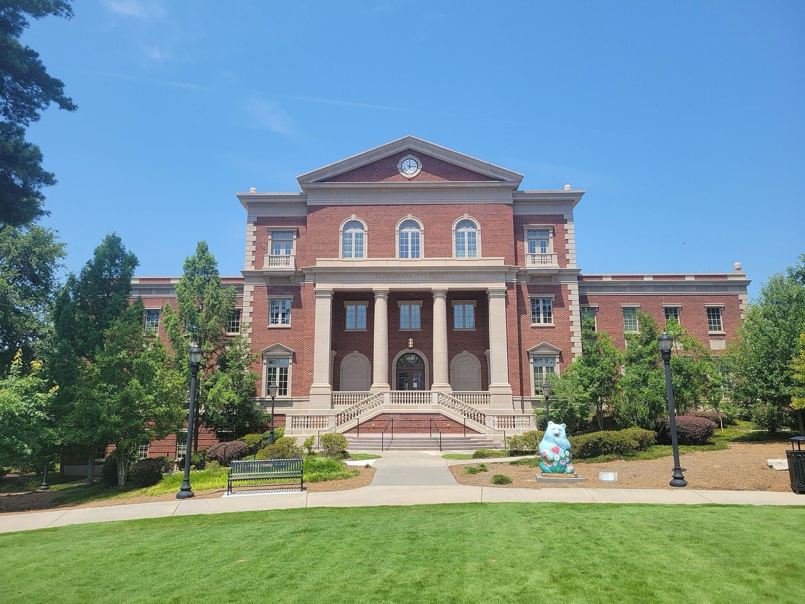 Alpharetta City Hall, a red-brick building with white columns, facing the lawn at Alpharetta City Center on a clear summer day