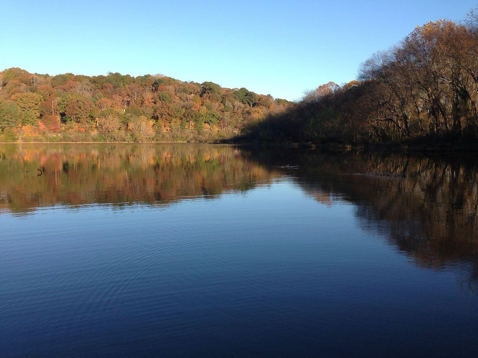 The calm Chattahoochee River at Roswell reflecting a blue sky and hills of orange and red fall leaves