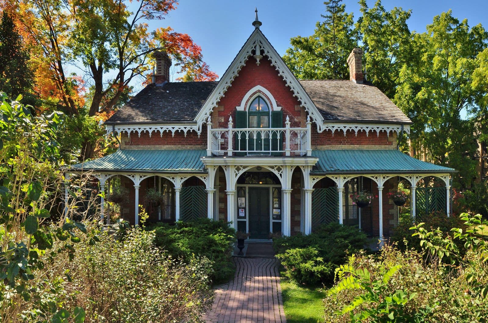 Hillary House in Aurora, a red-brick Gothic house with white gingerbread trim, a pointed central gable and a wide veranda, framed by autumn trees and garden beds