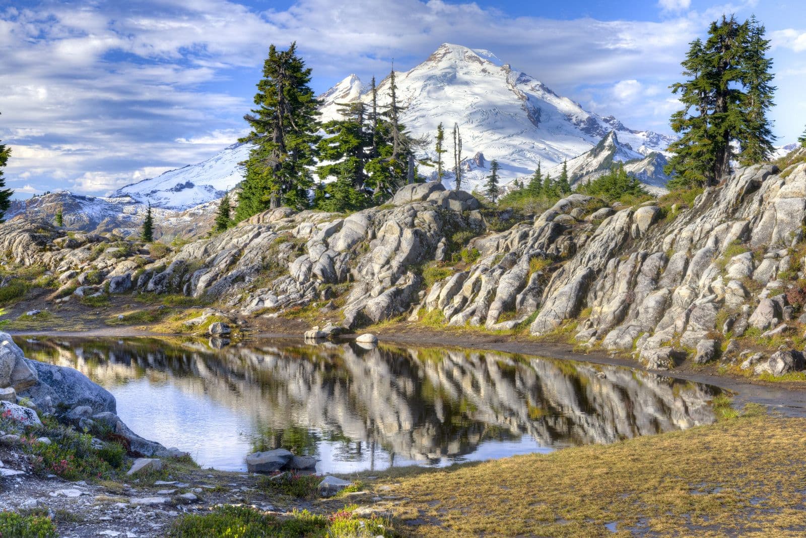 Glaciated Mount Baker reflected in a small alpine tarn below pale granite ledges and subalpine firs at Heather Meadows in early fall