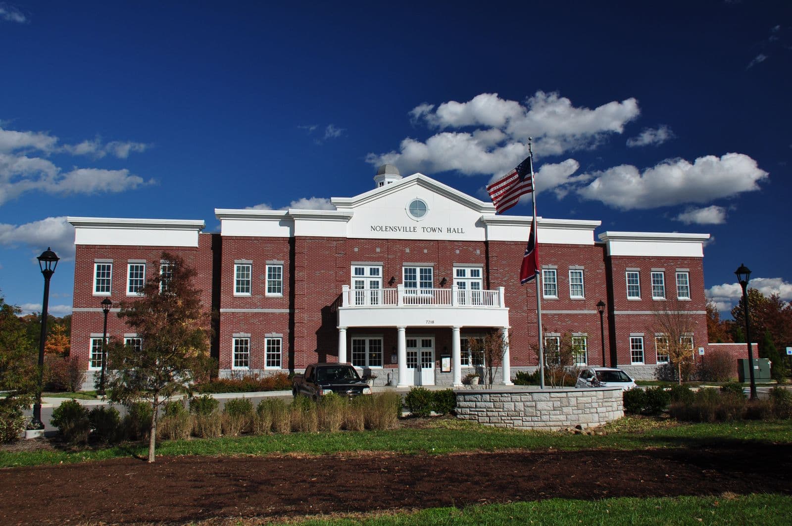Nolensville Town Hall, a two-story red-brick building with a white portico and balcony, under a deep blue fall sky