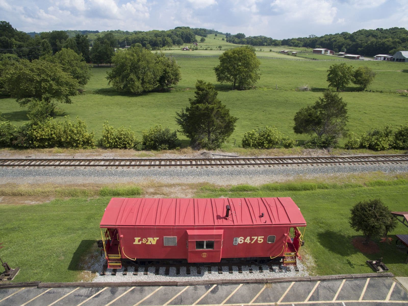 Aerial view of a red L&N caboose beside the railroad in Thompson’s Station, with the green pastures of Preservation Park and wooded hills behind