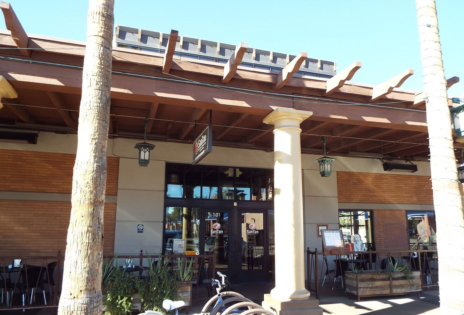 The 1913 Chandler Bank building on San Marcos Place in downtown Chandler, its shaded sidewalk patio set with tables under palm trees and a pergola