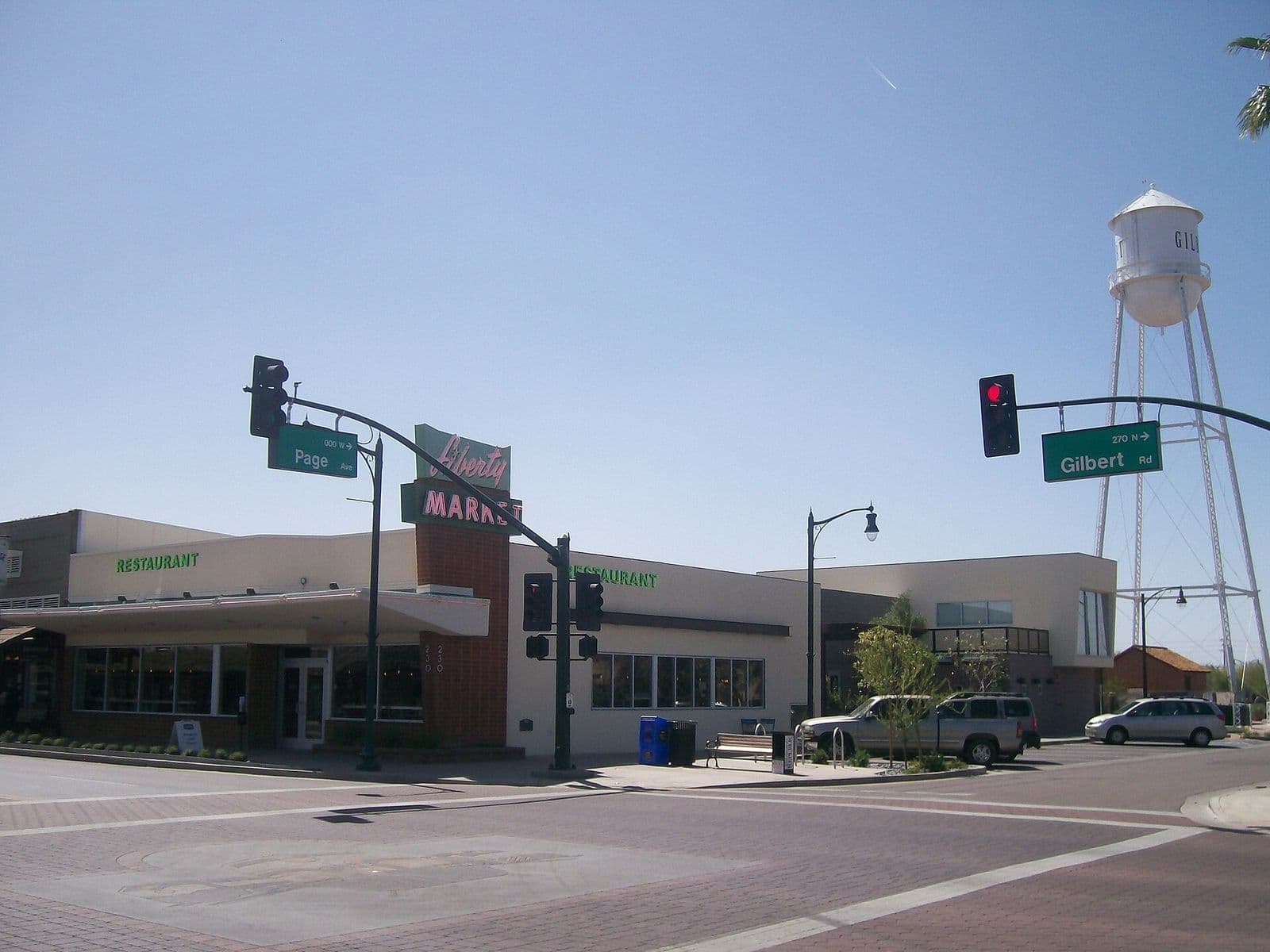 The corner of Gilbert Road and Page Avenue in downtown Gilbert, with the Liberty Market restaurant and the white Gilbert water tower rising behind under a clear blue sky