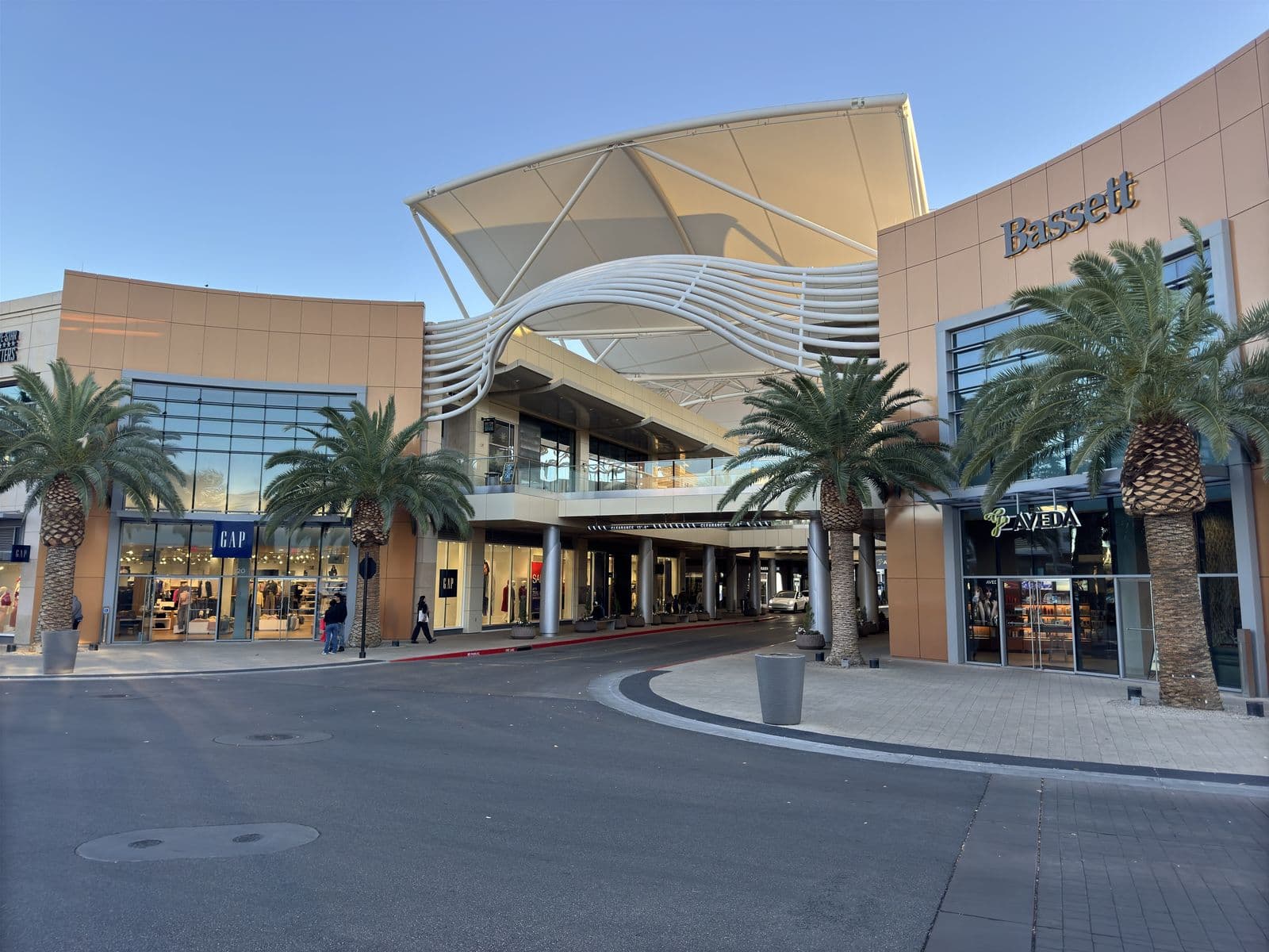 The open-air promenade of Downtown Summerlin at golden hour, with a sculptural white canopy over the walkway, palm trees and storefronts