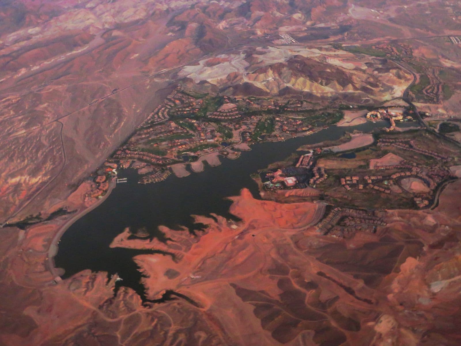 Lake Las Vegas at dusk from the air: the full reservoir ringed by resort villages and golf greens, with red desert hills all around