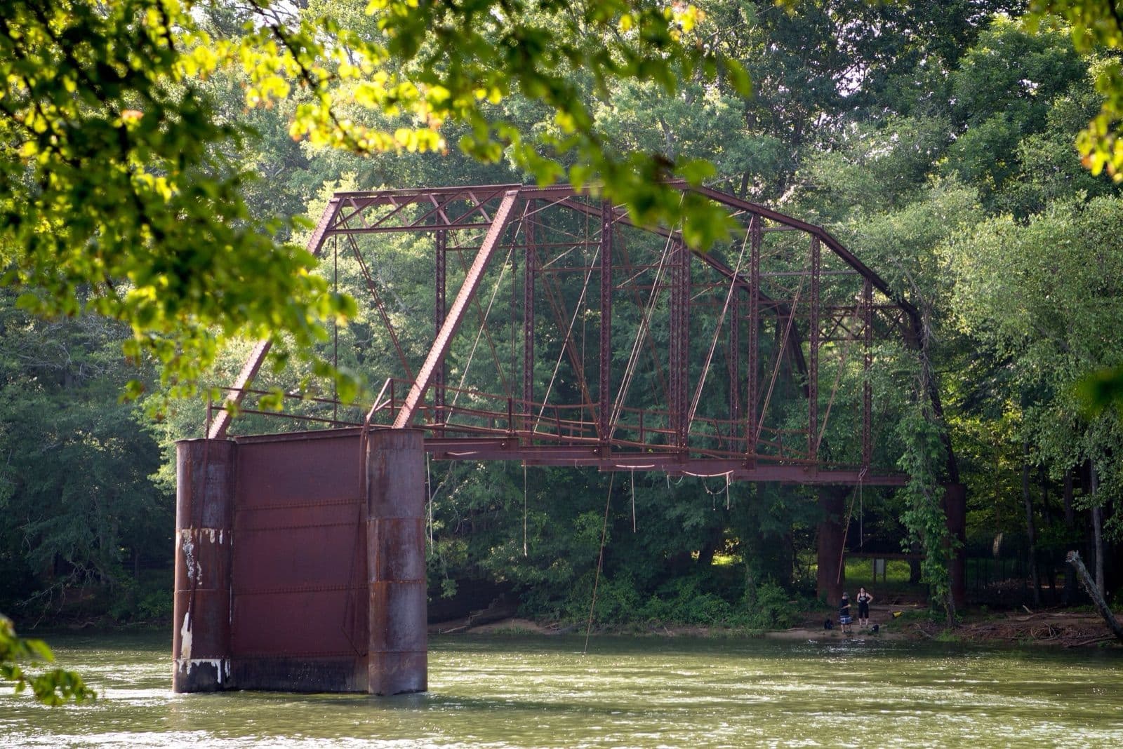 The rusted remaining span of the old Jones Bridge over the Chattahoochee River, framed by summer leaves