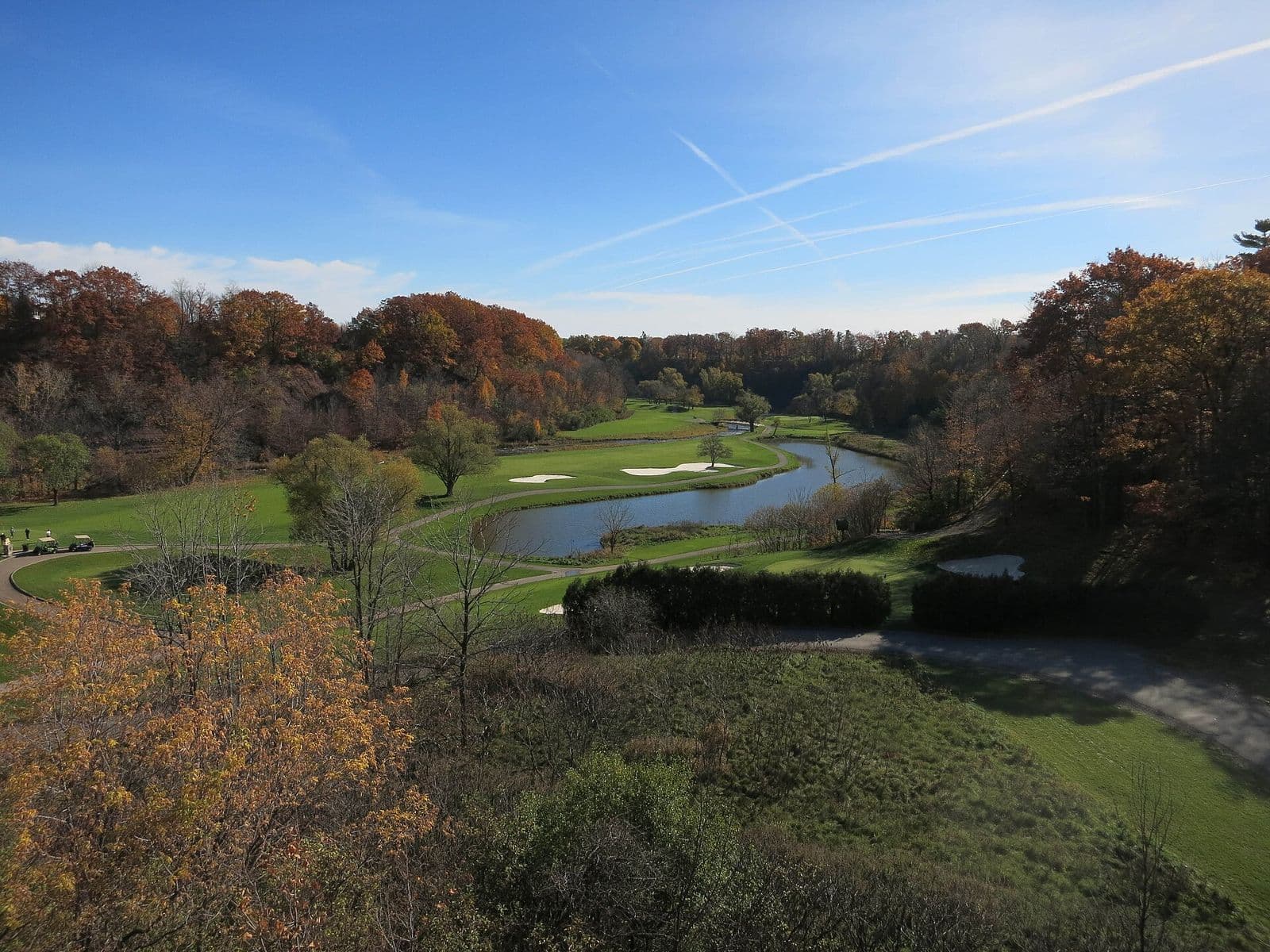 The Glen Abbey golf course in its creek valley in autumn, with a winding pond, sand bunkers and fairways below wooded slopes turning orange and red