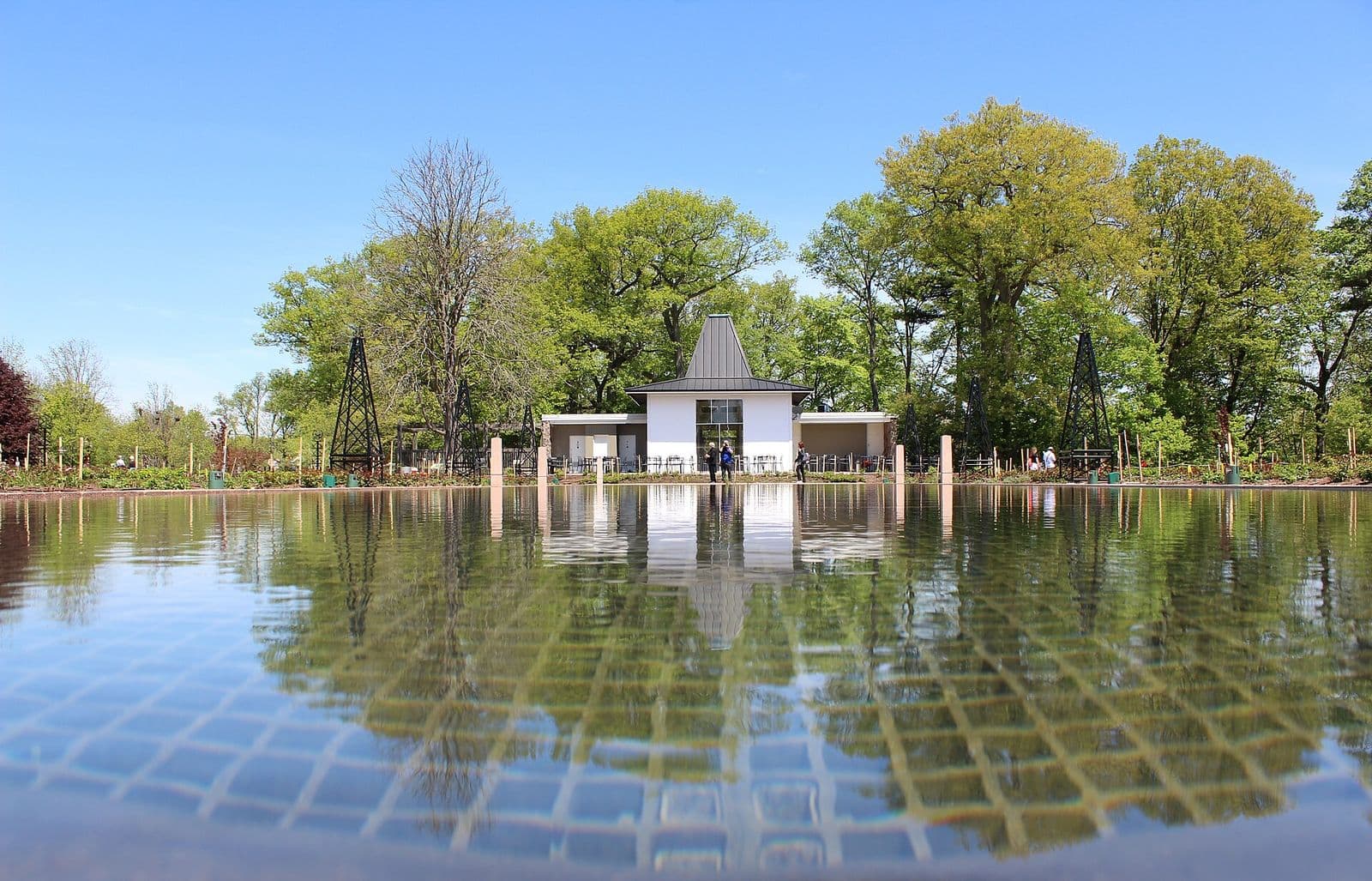 A white pavilion and tall spring trees reflected in the still reflecting pool of Hendrie Park at Royal Botanical Gardens in Burlington