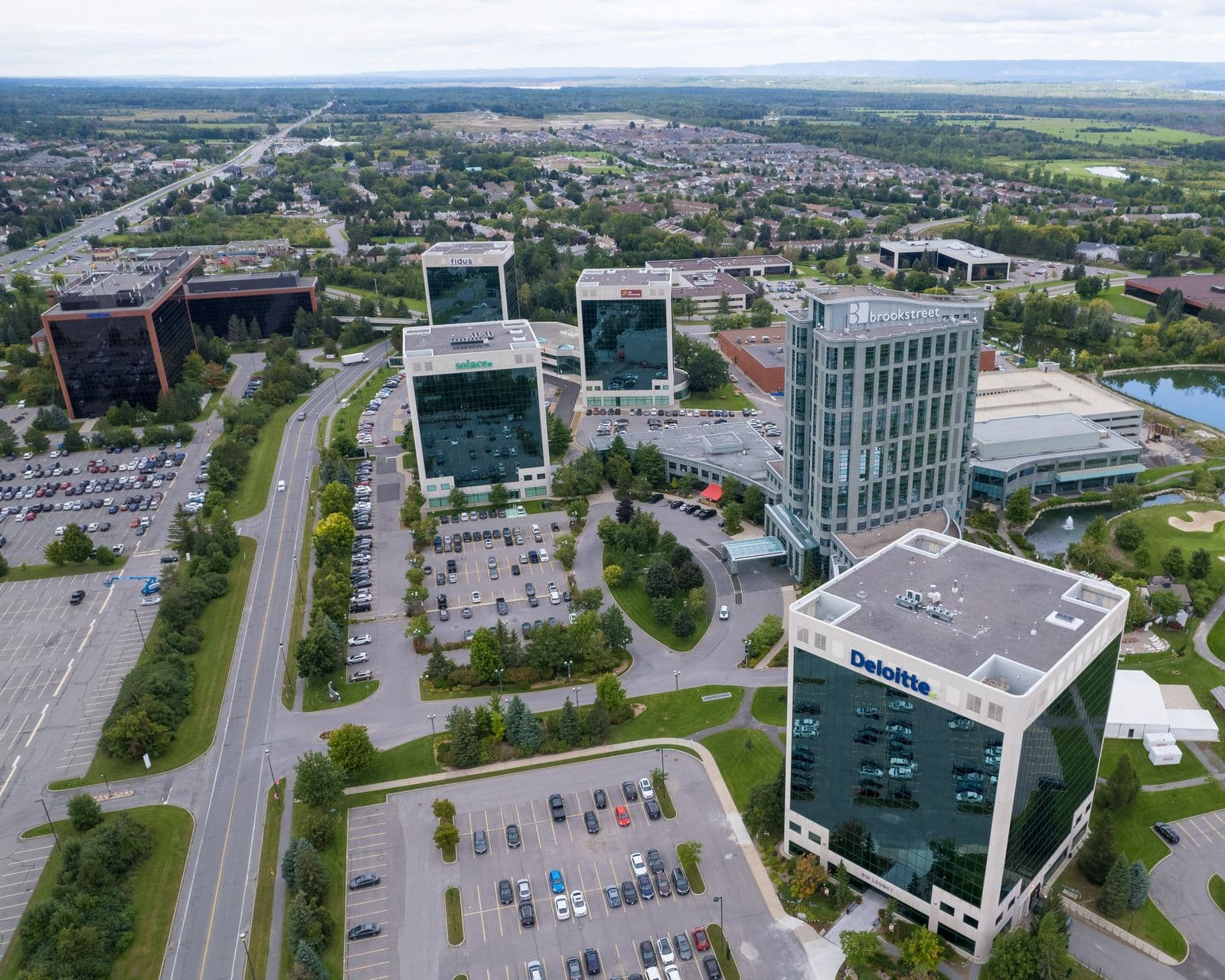 Aerial view of glass office towers and a hotel tower in the Kanata North technology park, with tree-lined streets of houses stretching to the horizon
