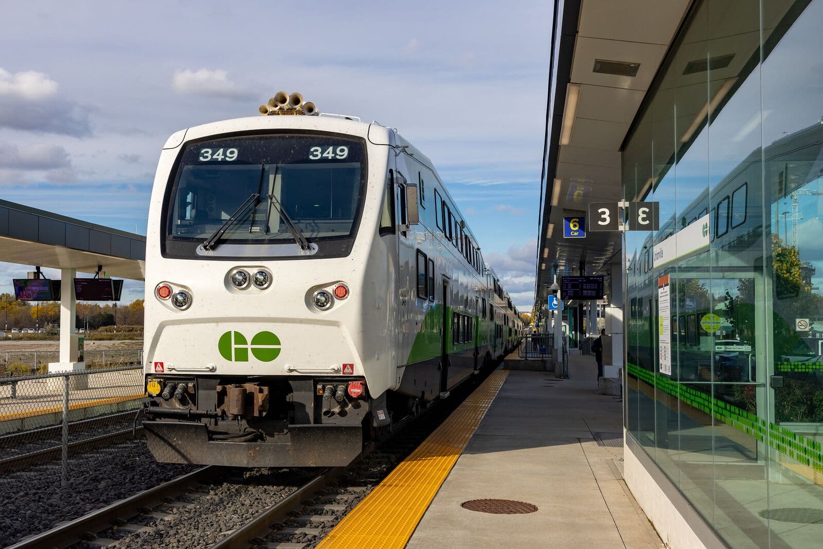 A white and green GO train on the Stouffville line waiting at the platform of Unionville GO Station on a bright autumn afternoon