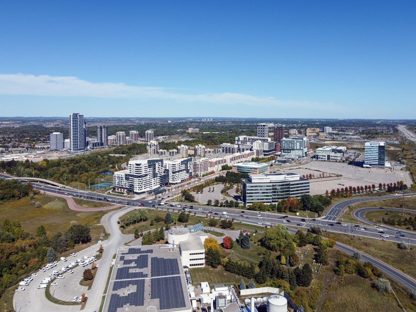 Aerial view of the condo towers and office buildings of downtown Markham on a clear early-autumn day, with a wide arterial road, green space and a few turning trees in front