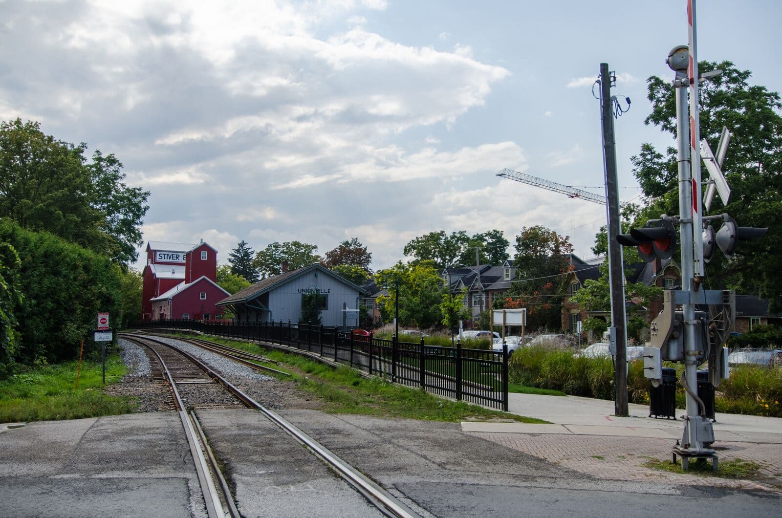 The red Stiver Mill and the grey wooden Unionville railway station beside the tracks at Station Lane in Unionville, under a partly cloudy late-summer sky