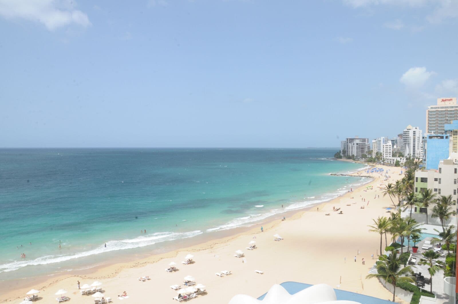 Condado Beach from a hotel high above: turquoise water, a long sand beach with white umbrellas and a row of condominium and hotel towers along the shore