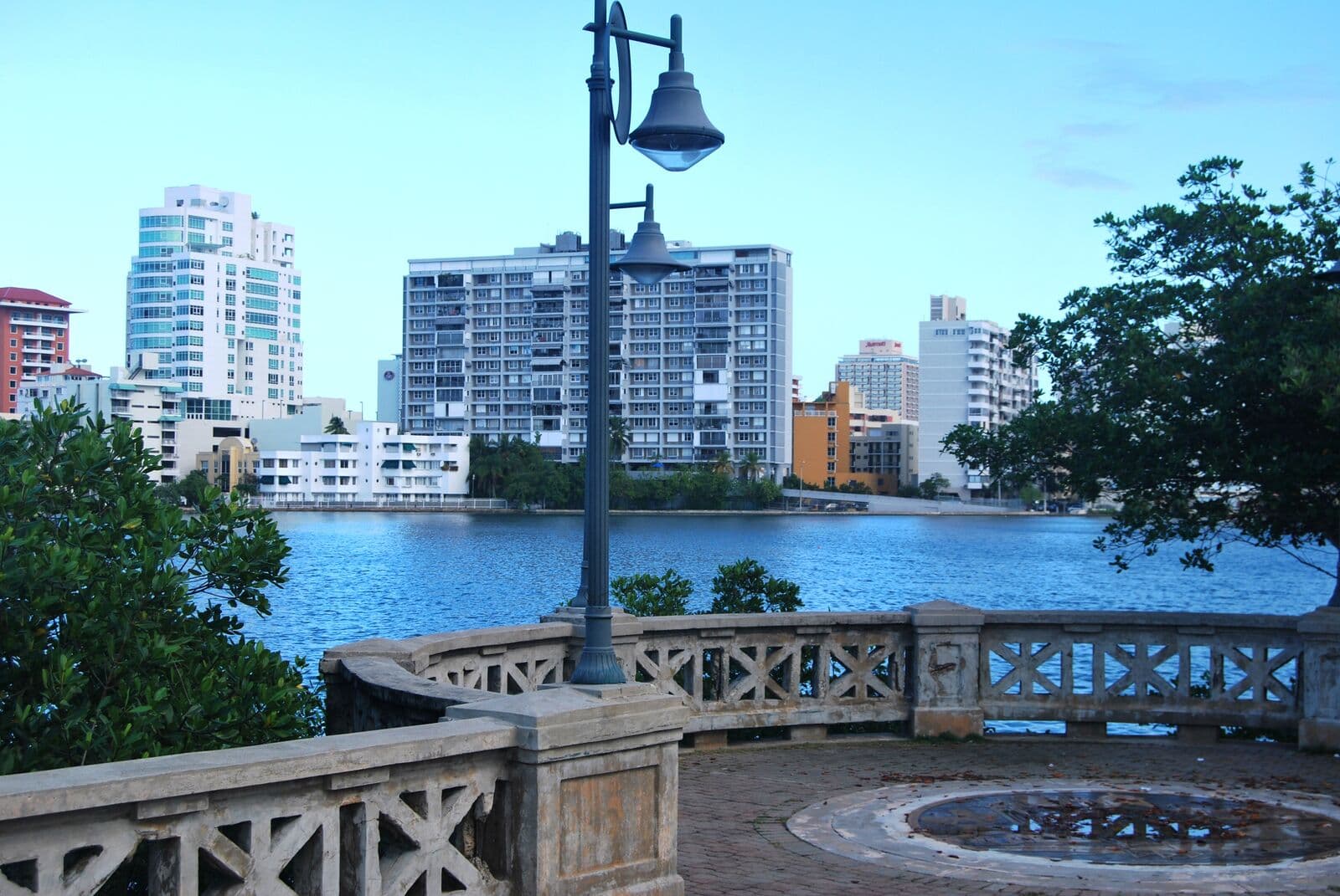 Torres de condominios frente a la Laguna del Condado, azul y tranquila, vistas desde un mirador de piedra con un farol y mangles