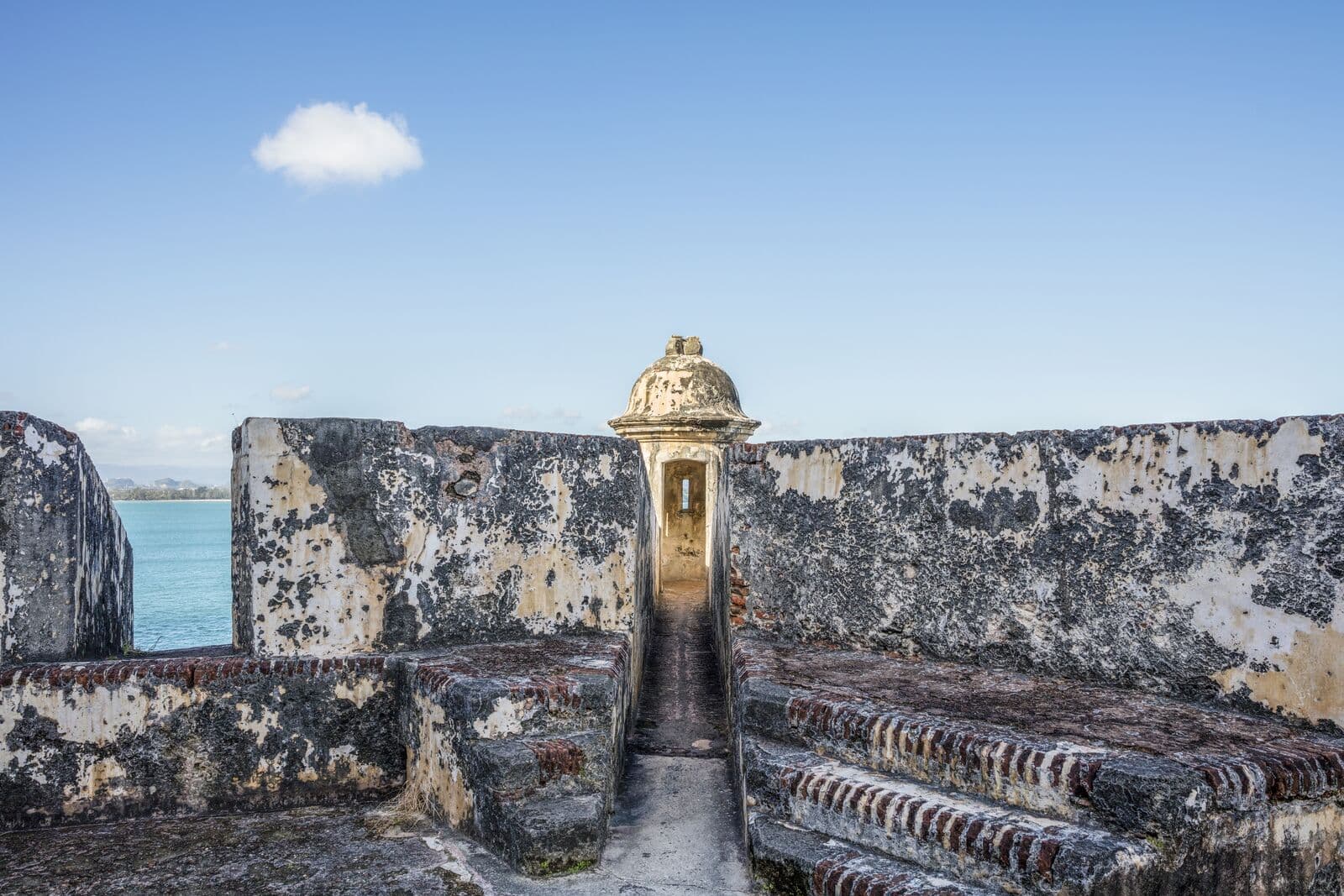 Una garita de piedra con cúpula en las murallas gastadas del Castillo San Felipe del Morro, con el mar y un cielo azul al fondo