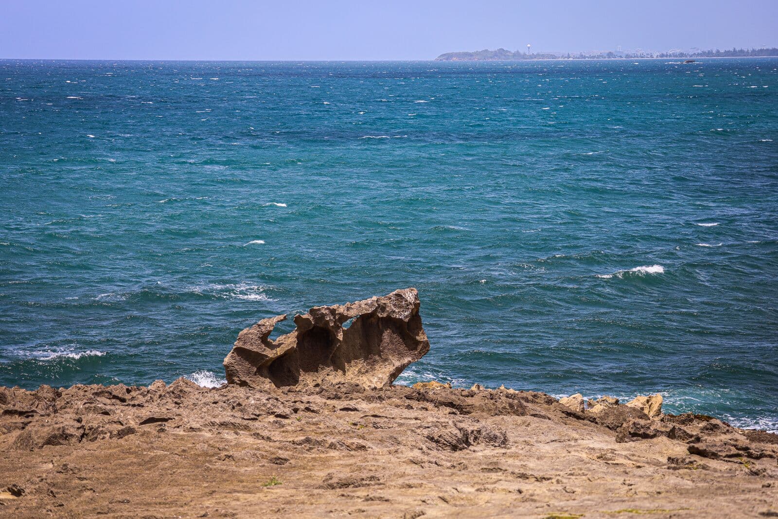 La roca caliza esculpida del Ojo del Buey en la costa rocosa de Dorado, sobre un mar azul verdoso picado con Punta Salinas a lo lejos