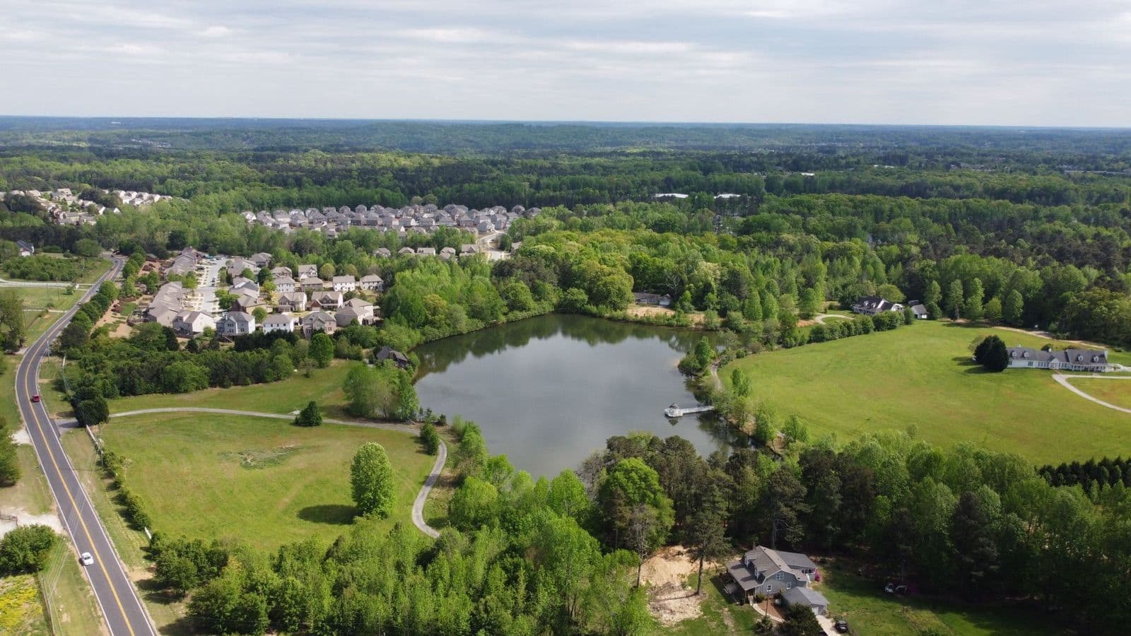 Aerial view of wooded Gwinnett County subdivisions near Buford around a pond with a small dock and open pasture