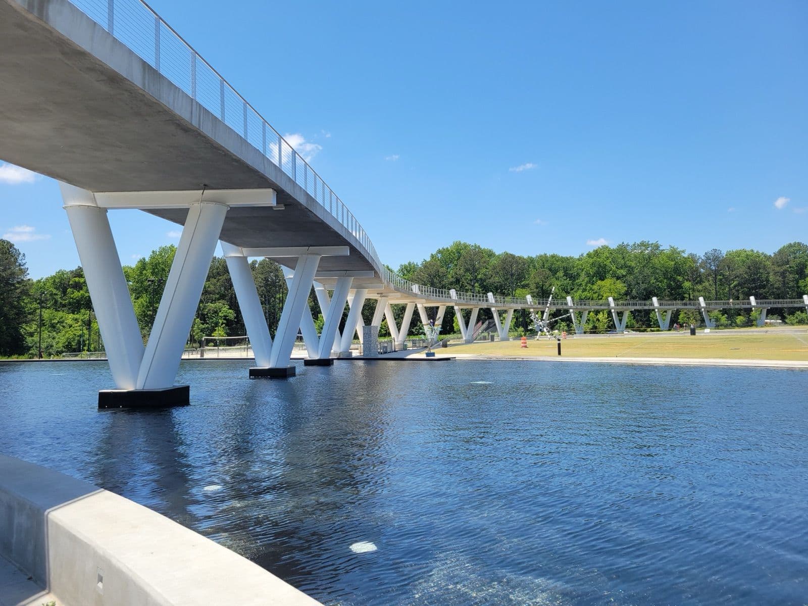 The white pedestrian bridge on V-shaped columns curving over the reflection pond and lawn at Town Center on Main in Suwanee
