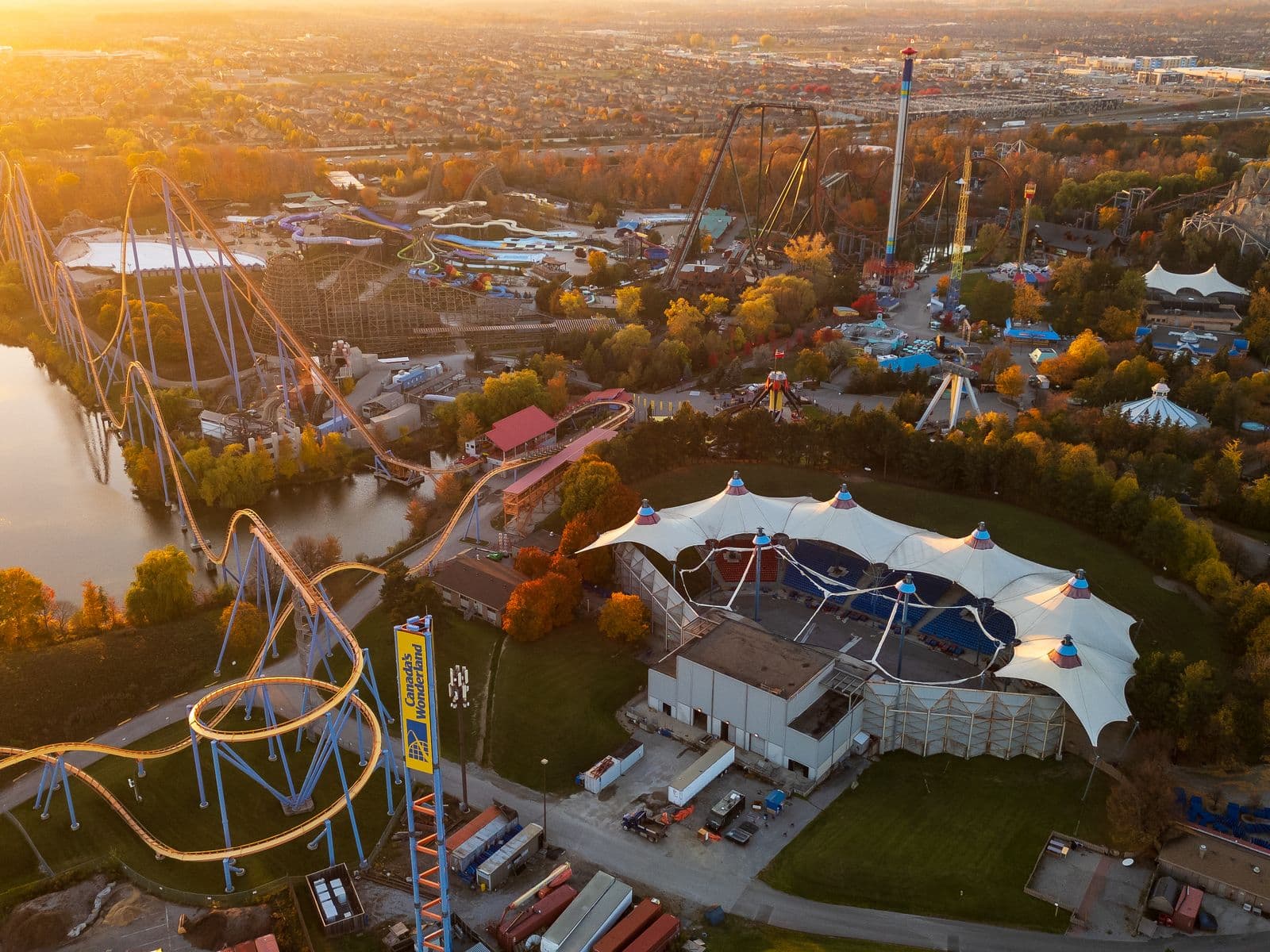 Aerial view of Canada’s Wonderland at sunset in autumn, its roller coasters, water slides and amphitheatre ringed by trees in fall colour, with rows of Vaughan subdivisions stretching to the horizon