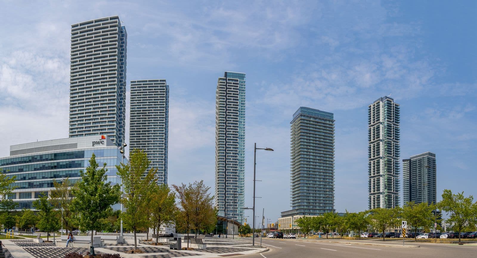 New condominium towers and an office building rise above young trees and a paved plaza in the Vaughan Metropolitan Centre on a summer day