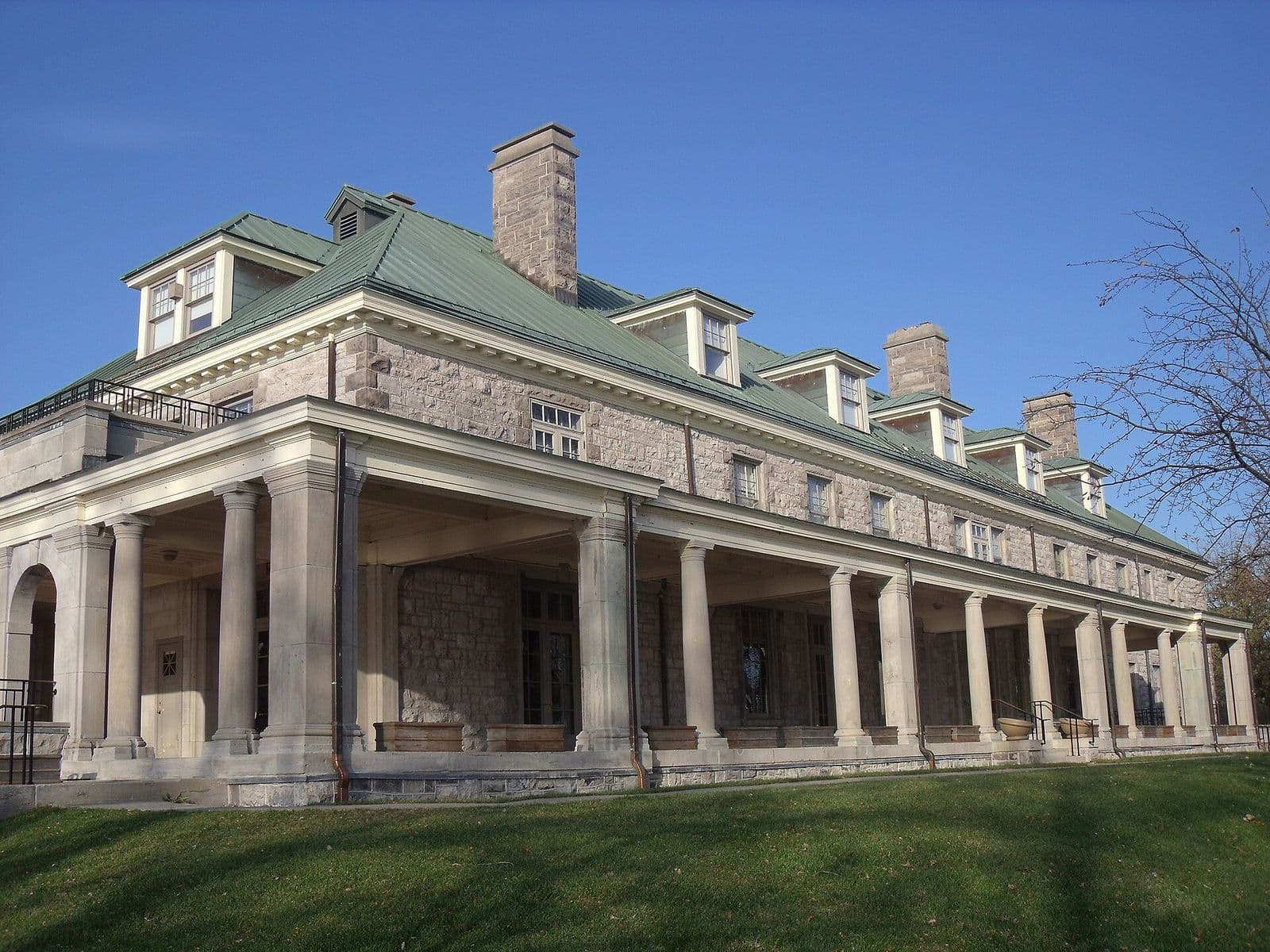 La longue colonnade de pierre, le toit de métal vert et les lucarnes de Stewart Hall sur sa pelouse, à Pointe-Claire, sous un ciel bleu profond